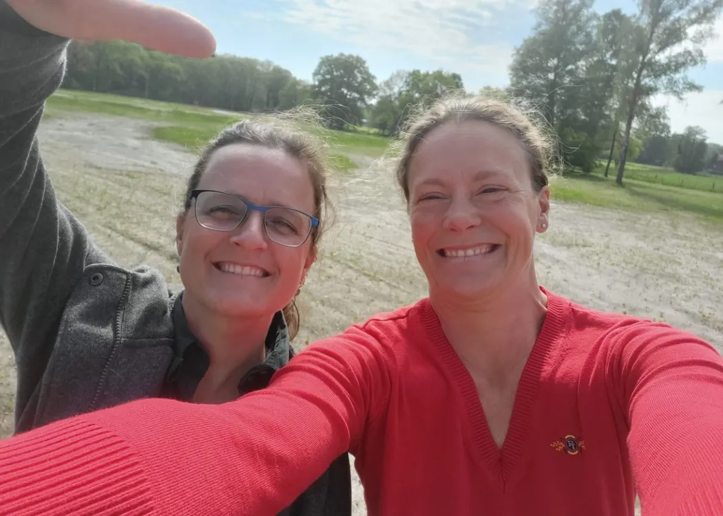 Selfie von zwei Frauen auf einer Wiese, vermutlich Baugrundstück der Tierarztpraxis Hohne im Harzklint. Eine Frau trägt eine graue Jacke, die andere einen roten Pullover beide lachen in die Kamera.