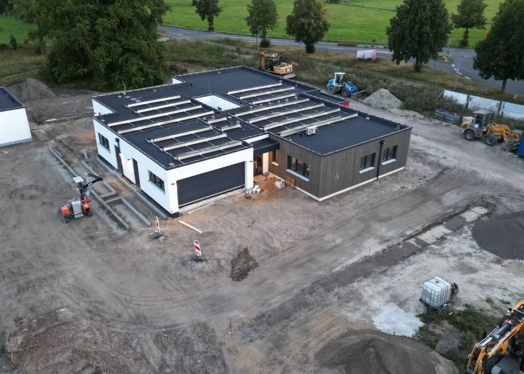 Bauphase der Tierarztpraxis Hohne im Harzklint. Luftaufnahme einer Baustelle mit teilweise fertiggestelltem Gebäude, sichtbarer Dachkonstruktion und Baugeräten auf unbefestigtem Gelände.