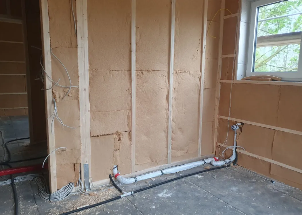 Innenaufnahme eines Rohbaus der Tierarztpraxis Hohne im Harzklint. Offene Wände mit Holzständerwerk und sichtbaren Wasserleitungen, ein Fenster gibt Blick nach draußen frei.