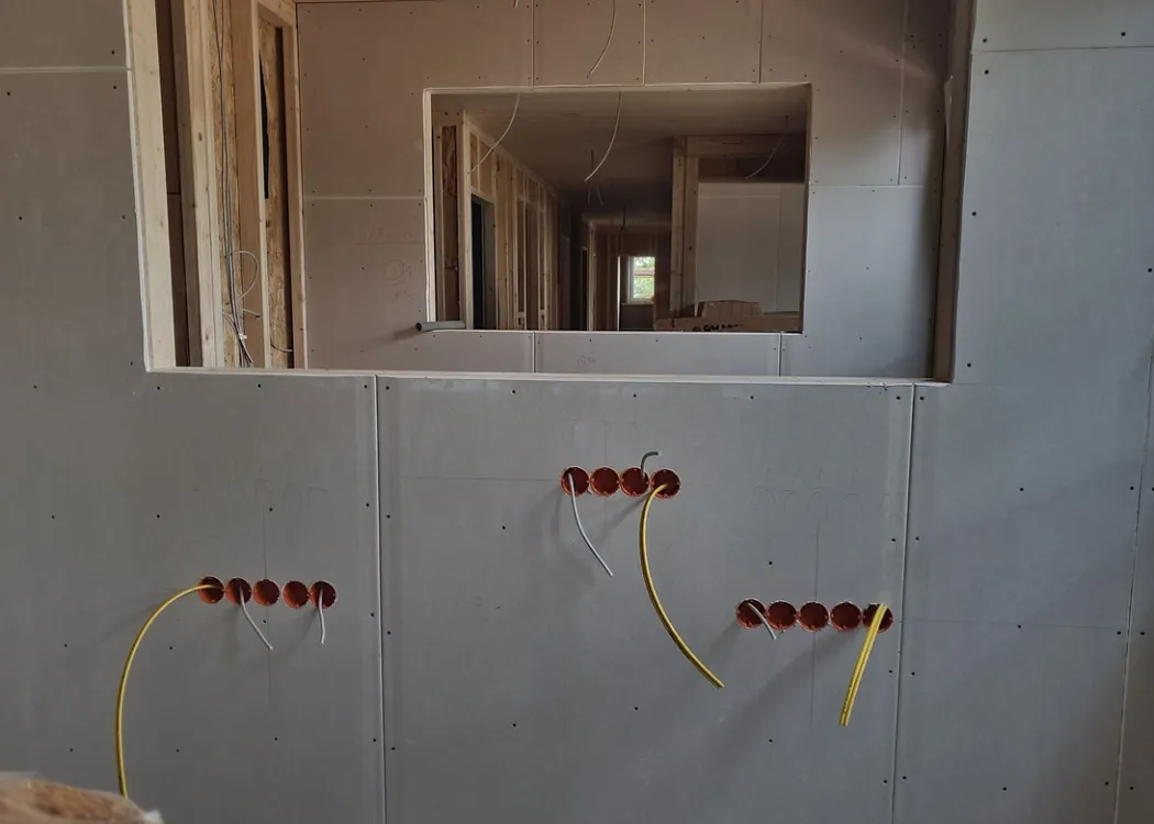 Innenraum der Tierarztpraxis Hohne im Harzklint im Rohbauzustand. Blick durch eine Wandöffnung auf einen langen Flur, in den Wänden sind bereits Steckdosen und Kabeldurchführungen vorbereitet.