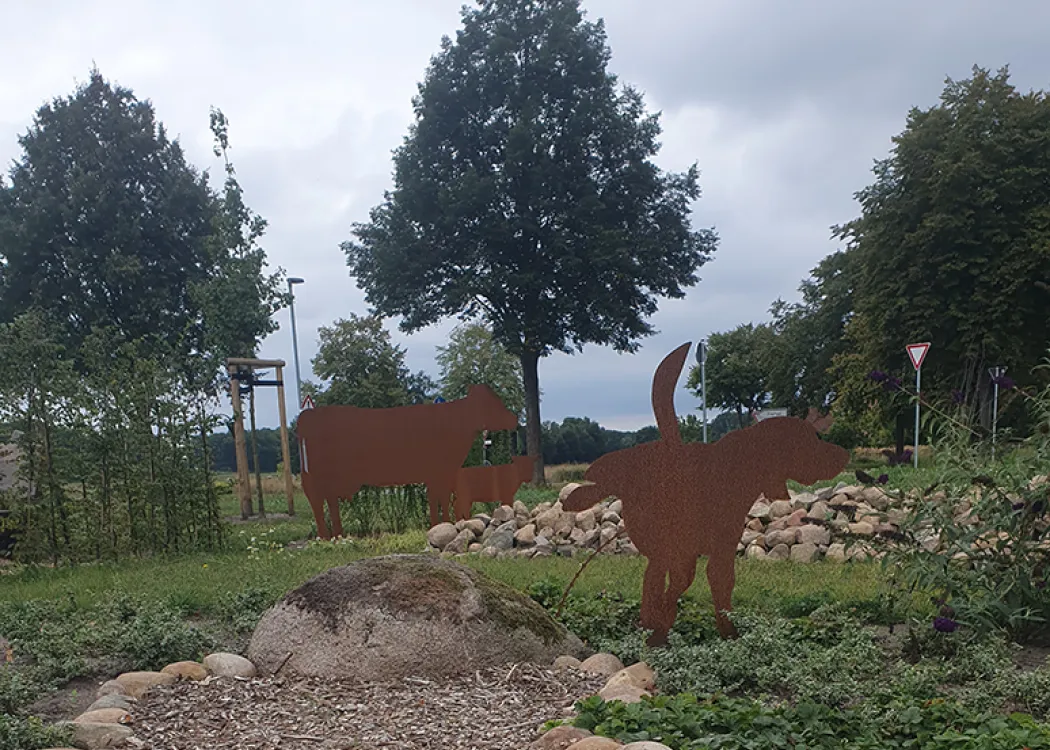 Dekorative Außenanlage der Tierarztpraxis mit Metallfiguren von Tieren auf einem Steingarten, umgeben von Bäumen und Grünfläche.