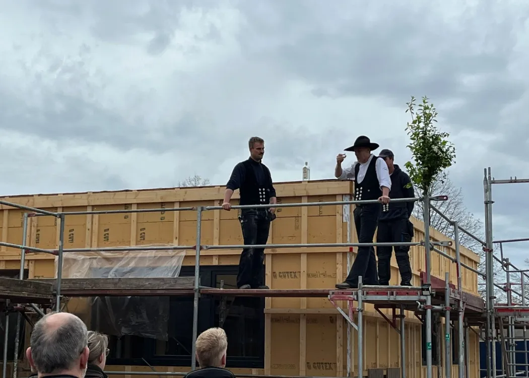Richtfest auf der Baustelle der Tierarztpraxis Hohne im Harzklint. Mehrere Personen in traditioneller Zimmermannskleidung stehen auf dem Holzgerüst, Zuschauer beobachten von unten. Im Hintergrund wolkiger Himmel.