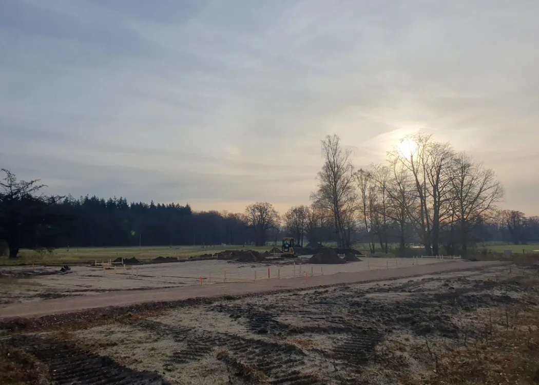 Weitwinkelaufnahme des Baugrundstücks der Tierarztpraxis Hohne im Harzklint. Ein freies Feld mit aufgeschütteter Sandplatte, die für den Bau vorbereitet wird. Winterliche Stimmung mit kahlen Bäumen und tief stehender Sonne.