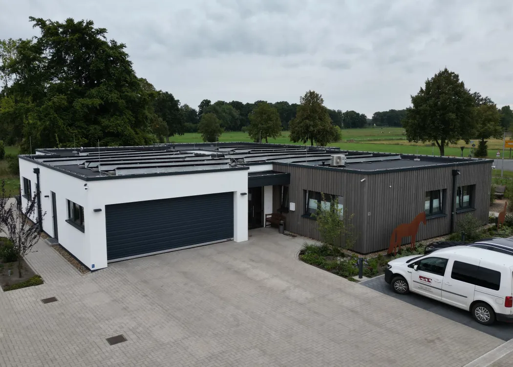 Seitenansicht der Tierarztpraxis mit weißer und grauer Fassade, angrenzender Einfahrt und parkendem Fahrzeug vor dem Gebäude.