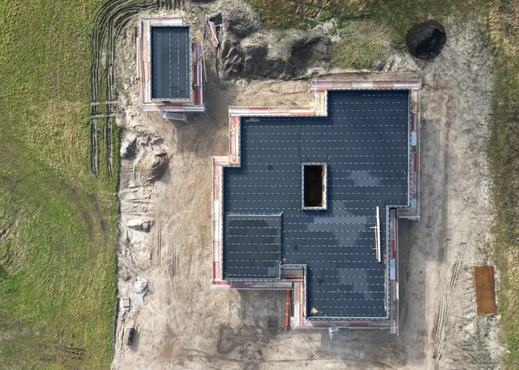 Luftaufnahme der Baustelle der Tierarztpraxis Hohne im Harzklint. Das Gebäude hat bereits ein dunkles Dach, die Wände stehen, und die Grundform mit Anbauten ist klar erkennbar. Ringsherum unbefestigtes Erdreich.