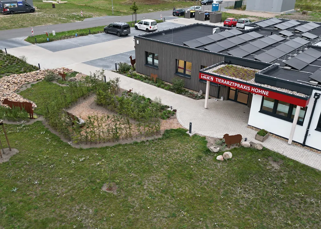 Moderne Tierarztpraxis in eingeschossiger Bauweise mit Flachdach und Solarpaneelen, umgeben von Grünflächen und einem gepflasterten Vorplatz.