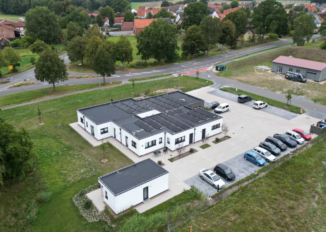 Übersichtsfoto der Praxisanlage mit mehreren Parkplätzen, modernem Praxisgebäude und umliegenden Häusern im Hintergrund.