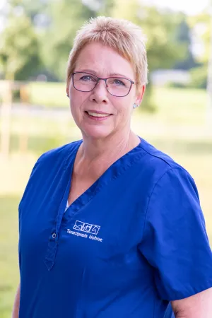 Frau mit blonden, kurzen Haaren trägt ein blaues Arztkittel mit dem Logo 'Tierarztpraxis Hohne' auf der linken Brustseite.